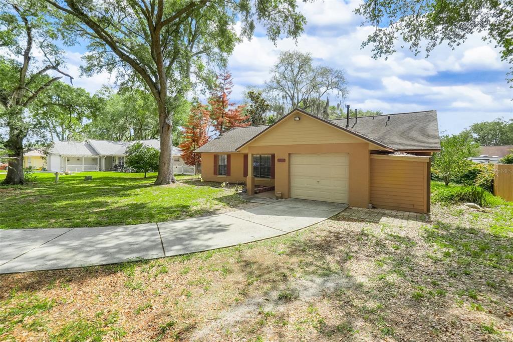 A single-story house with a tan exterior, a concrete driveway, and large shade trees — 207 HOWARD COURT, MASCOTTE, FL