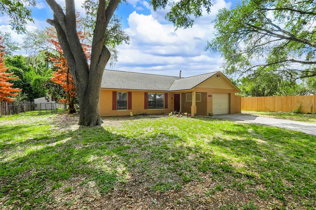 A single-story house with a tan exterior, brown shutters, and a garage sits on grass — 207 HOWARD COURT, MASCOTTE, FL