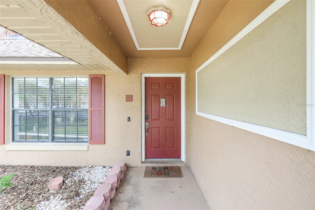 An exterior view of a home entrance featuring a red door and a covered porch — 207 HOWARD COURT, MASCOTTE, FL