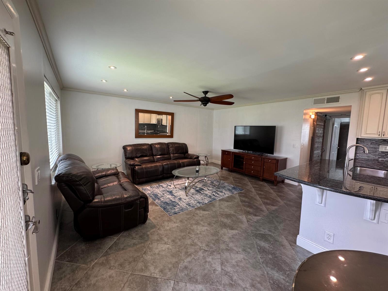 A living room with dark leather furniture, a glass coffee table, and tile flooring — 510 Flanders K, Delray Beach FL 33484, DELRAY BEACH, FL
