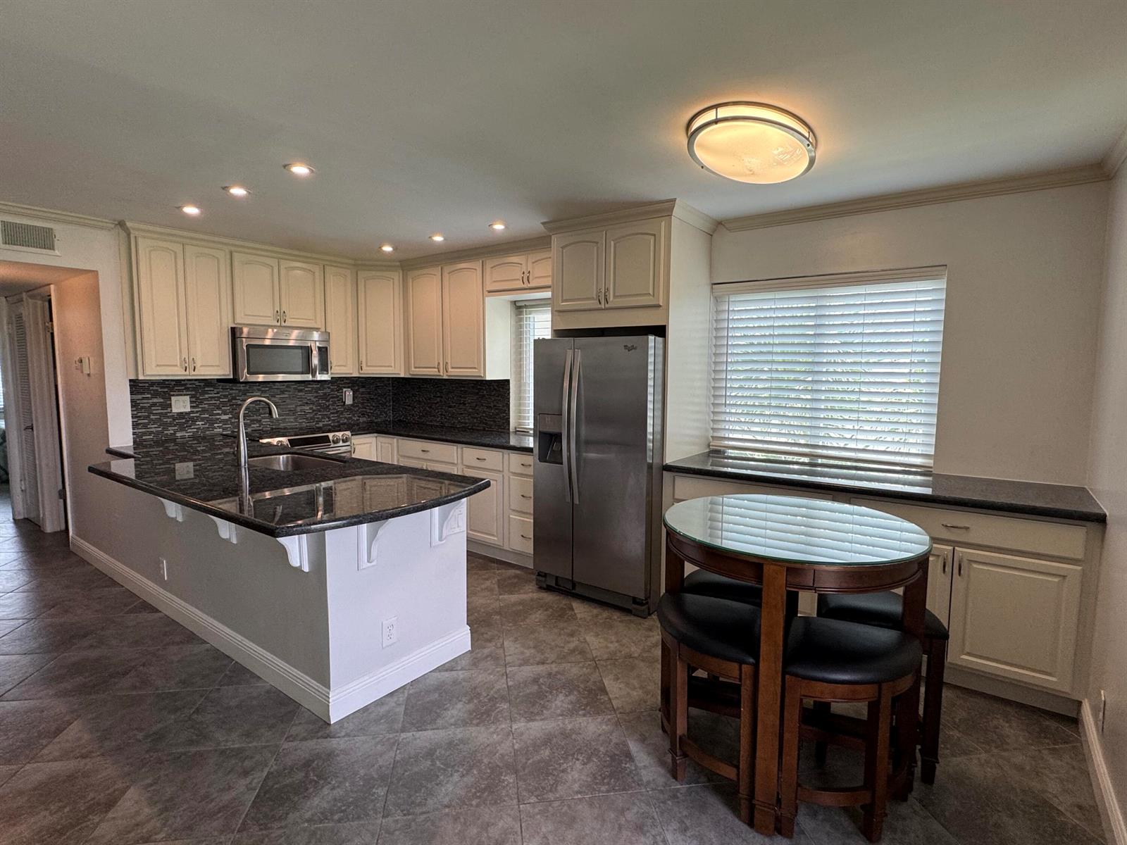 A kitchen with white cabinets, dark granite countertops, stainless steel appliances, and a dining table — 510 Flanders K, Delray Beach FL 33484, DELRAY BEACH, FL