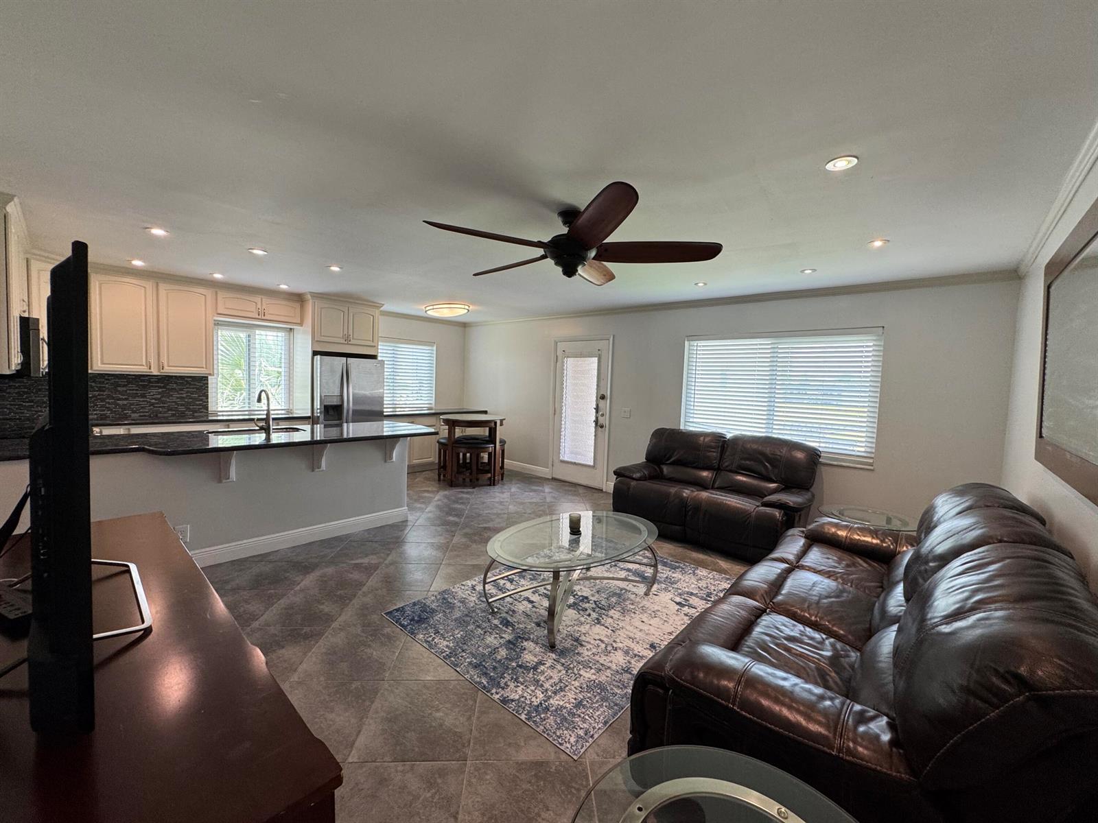 An open-concept living room and kitchen featuring dark leather furniture, tile flooring, and white cabinetry — 510 Flanders K, Delray Beach FL 33484, DELRAY BEACH, FL