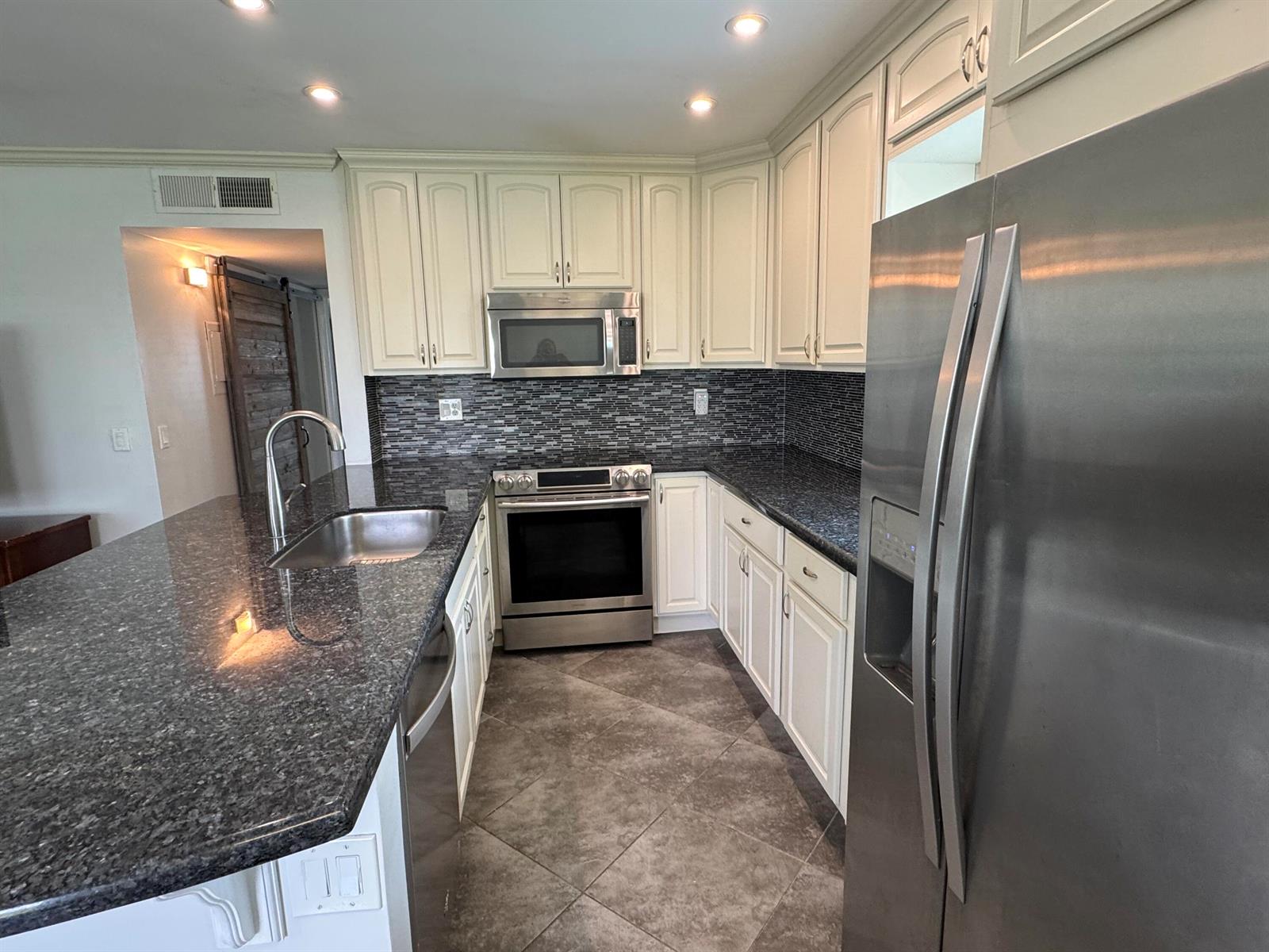 A kitchen features white cabinets, dark granite countertops, stainless steel appliances, and tiled flooring — 510 Flanders K, Delray Beach FL 33484, DELRAY BEACH, FL