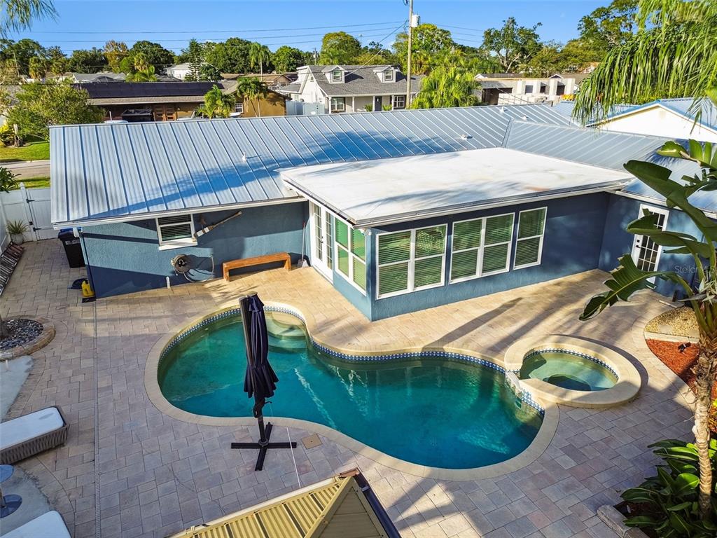 An aerial view of a blue house with a metal roof, pool, and paver patio — 8708 THORNWOOD LANE, TAMPA, FL