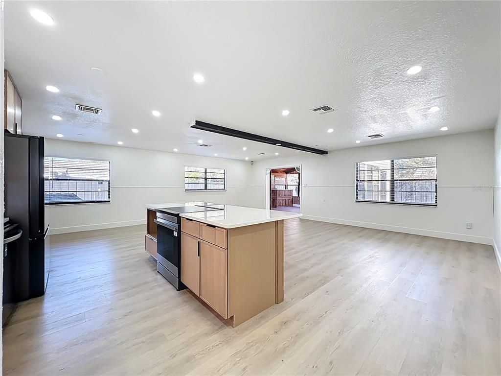 A kitchen island with a stove sits in a large, open-concept room with light flooring — 3463 ARNEL DRIVE, WINTER PARK, FL
