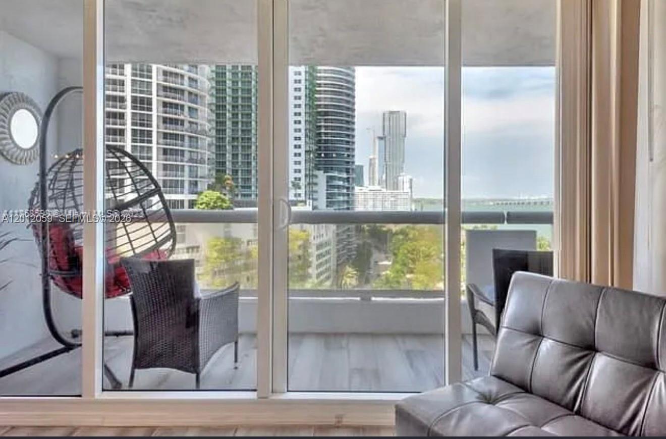 A living room with a leather sofa looks out through floor-to-ceiling windows onto a balcony — 1717 N Bayshore Dr # A1448, Miami FL 33132, MIAMI, FL
