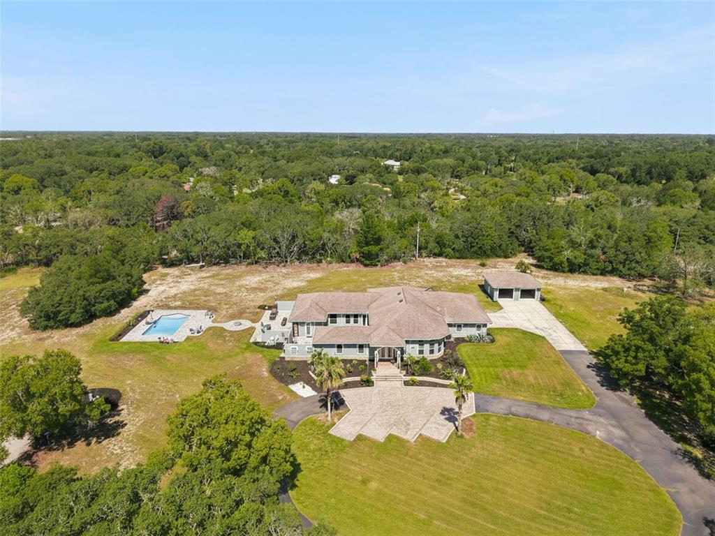 An aerial view shows a large house with a pool, detached garage, and paved driveway — 10030 ORCHARD WAY, SPRING HILL, FL