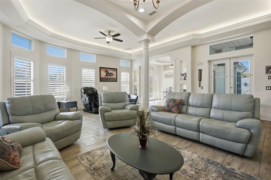 A spacious living room features light gray leather furniture, a central coffee table, and columns — 10030 ORCHARD WAY, SPRING HILL, FL
