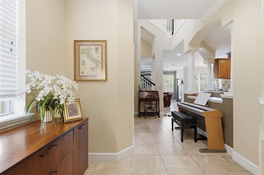 A foyer with tile flooring leads to a living area featuring a piano and staircase — 2656 TANGLEWOOD TRAIL, PALM HARBOR, FL