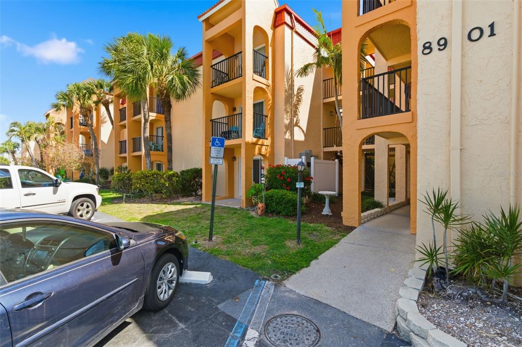 An exterior view of a multi-story apartment building with balconies, palm trees, and parking — 8901 BLIND PASS ROAD UNIT 127, ST PETE BEACH, FL