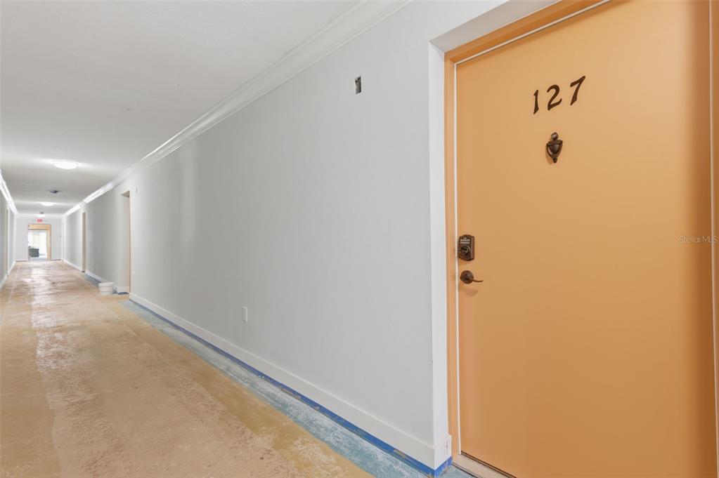 A long hallway features a light-colored door numbered 127 and unfinished concrete flooring — 8901 BLIND PASS ROAD UNIT 127, ST PETE BEACH, FL