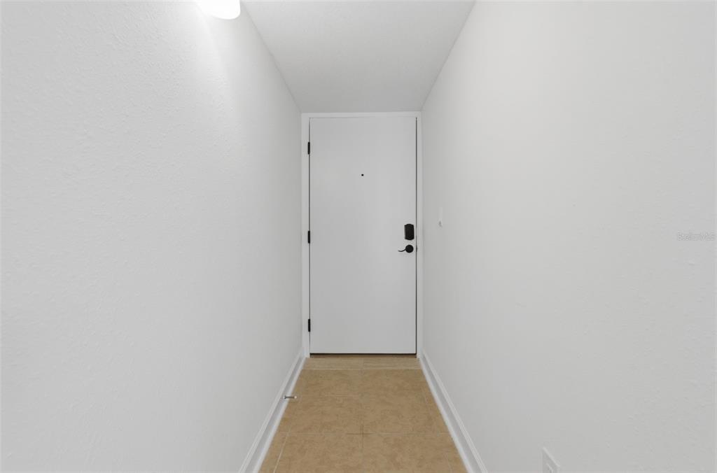 A narrow entryway features white walls, a tiled floor, and a single white door — 8901 BLIND PASS ROAD UNIT 127, ST PETE BEACH, FL