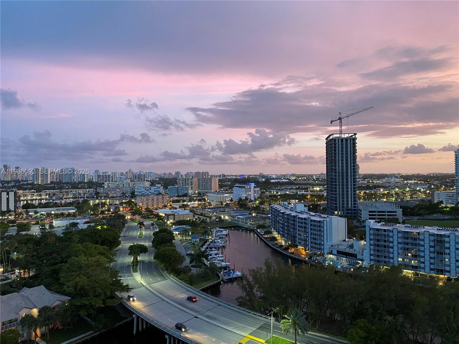 An elevated view of a city skyline at sunset featuring a canal, bridge, and construction crane — 300 Three Islands Blvd # 520, Hallandale Beach FL 33009, HALLANDALE BEACH, FL