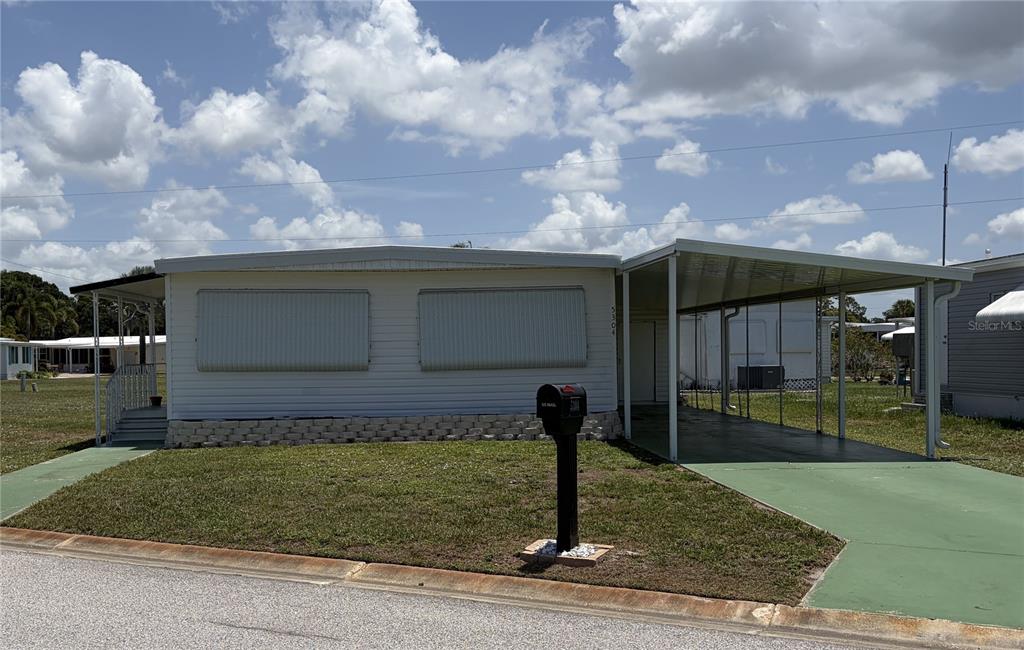 A single-story manufactured home with a carport, white siding, and a front lawn — 5304 CHERRY HILL AVENUE, SARASOTA, FL