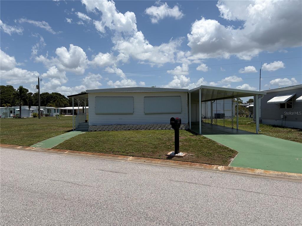A single-story manufactured home features a carport, green painted concrete, and a front lawn — 5304 CHERRY HILL AVENUE, SARASOTA, FL