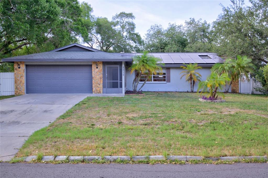 A single-story house with a gray garage, stone accents, and solar panels on the roof — 7312 S FITZGERALD STREET, TAMPA, FL