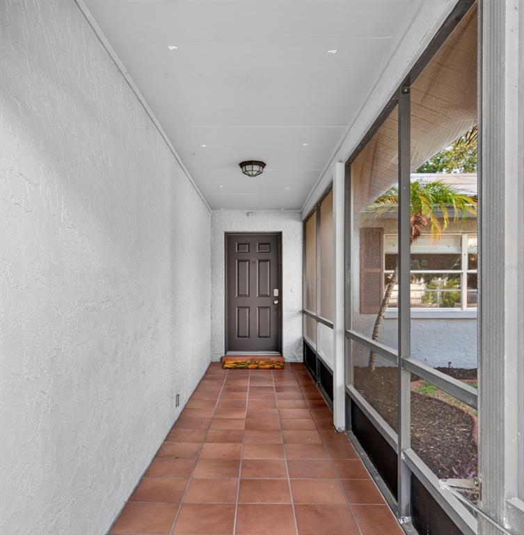 A covered, screened-in entryway features a brown front door and brown tiled flooring — 7312 S FITZGERALD STREET, TAMPA, FL
