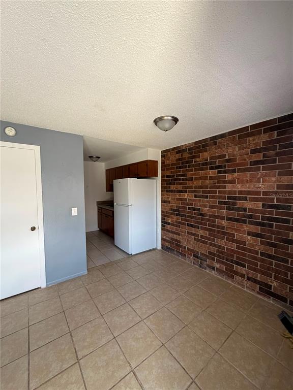 A kitchen area features a white refrigerator, brown cabinets, tile flooring, and a brick wall — 223 ORANGE STREET UNIT 1-6, AUBURNDALE, FL