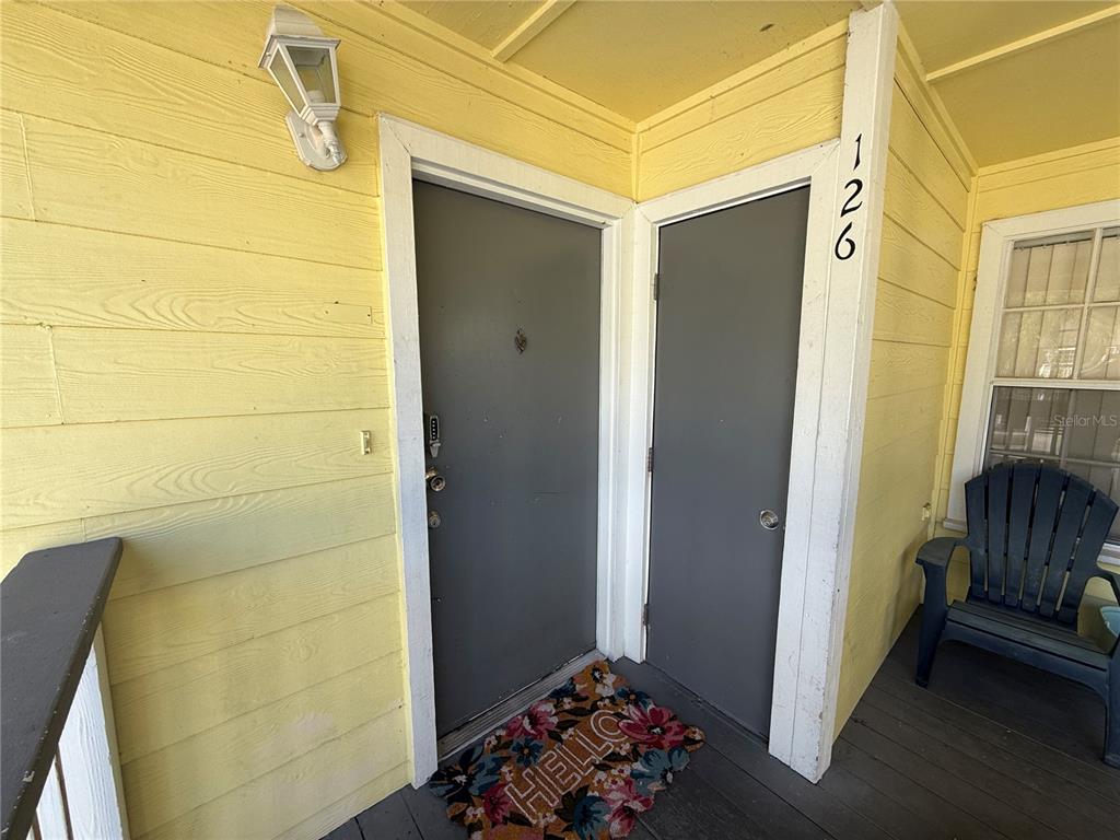 A yellow-sided porch features two gray doors, a floral welcome mat, and a dark chair — 2006 ROYAL BAY BOULEVARD UNIT 126, KISSIMMEE, FL