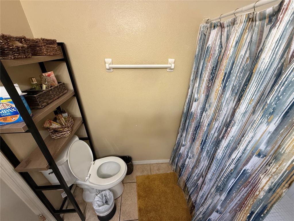 A bathroom features a toilet, a tall shelving unit, and a patterned shower curtain — 2006 ROYAL BAY BOULEVARD UNIT 126, KISSIMMEE, FL