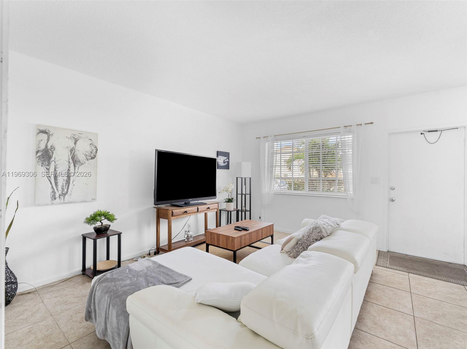 A living room features a white sectional sofa, a television on a wooden console, and tile flooring — 3220 NE 10th St # 5, Pompano Beach FL 3306, POMPANO BEACH, FL