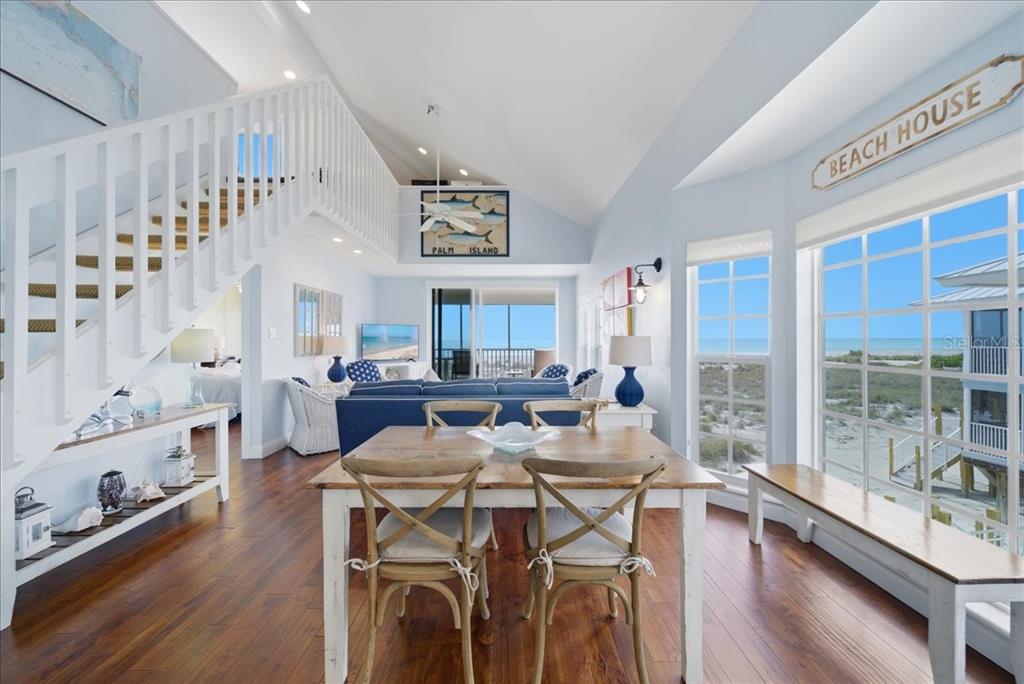 A dining area and living room with hardwood floors, a staircase, and large beach-facing windows — 7466 PALM ISLAND DRIVE UNIT 2922, PLACIDA, FL