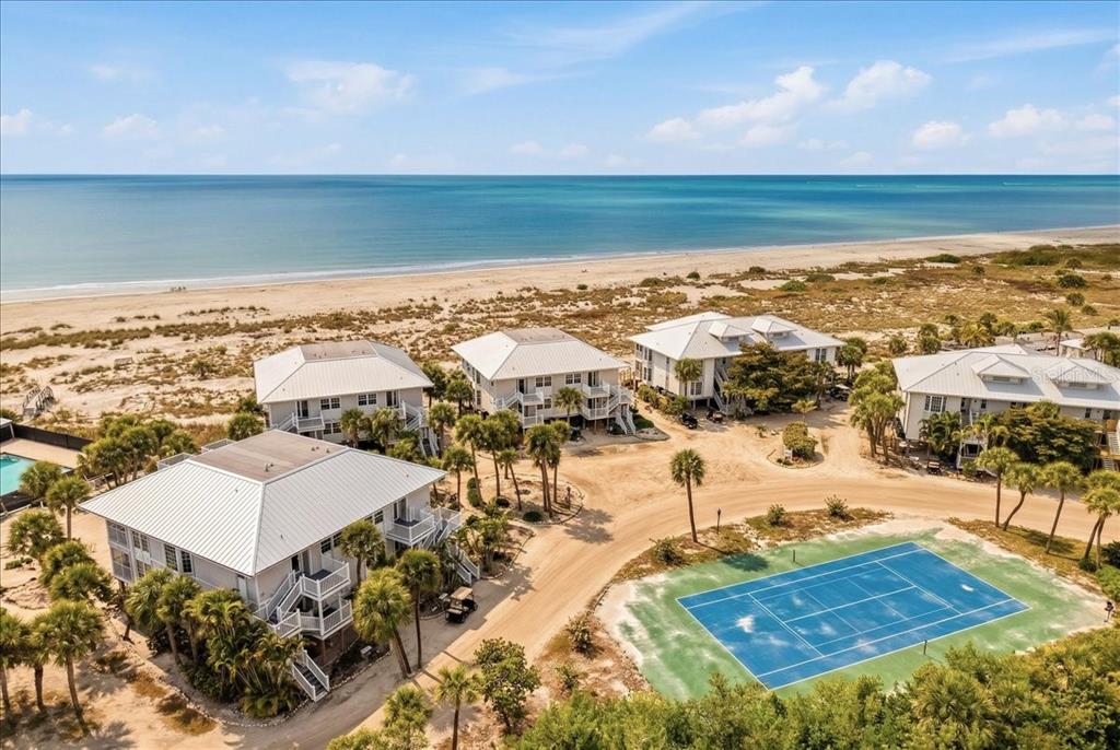 An aerial view shows several beach houses, a tennis court, and a sandy coastline — 7466 PALM ISLAND DRIVE UNIT 2922, PLACIDA, FL