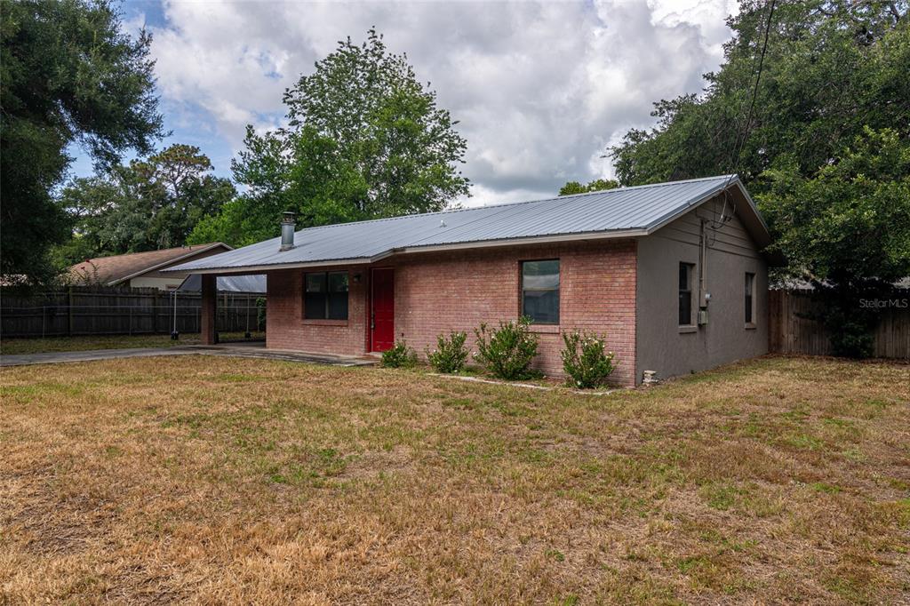 A single-story brick house features a metal roof, a red front door, and a carport — 6362 NW 64TH TERRACE, OCALA, FL