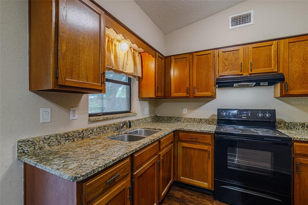 A kitchen features wood cabinets, granite countertops, and black appliances — 6362 NW 64TH TERRACE, OCALA, FL