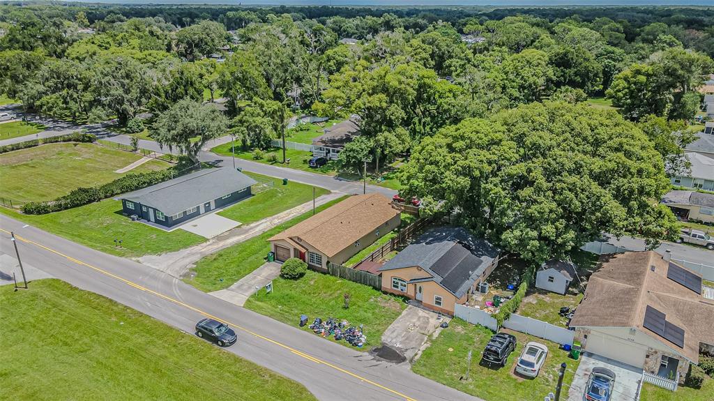 An aerial view shows several single-story houses along a road surrounded by mature trees — 5512 20TH STREET, ZEPHYRHILLS, FL