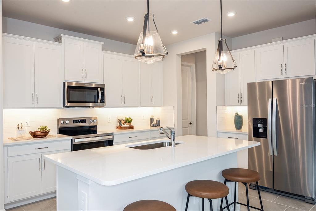 A modern kitchen features white cabinetry, stainless steel appliances, a central island, and pendant lighting — 34872 ARBOR RETREAT DRIVE, DADE CITY, FL