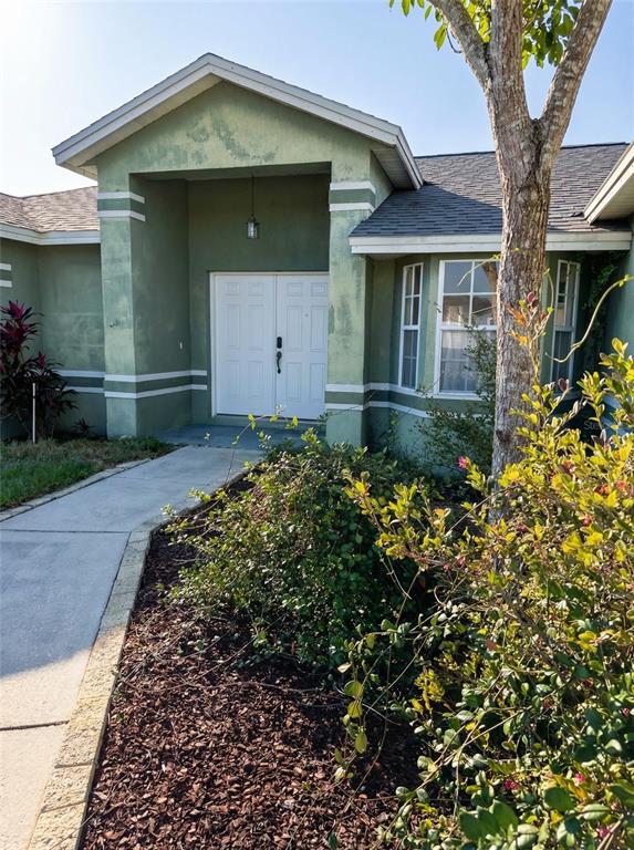 A green house exterior features a double front door, a walkway, and a landscaped yard — 702 TARTAN LOOP, LAKE WALES, FL