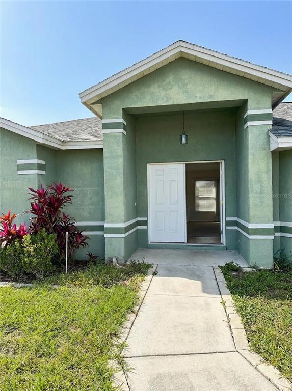The exterior of a green stucco house features a covered entryway and a concrete walkway — 702 TARTAN LOOP, LAKE WALES, FL