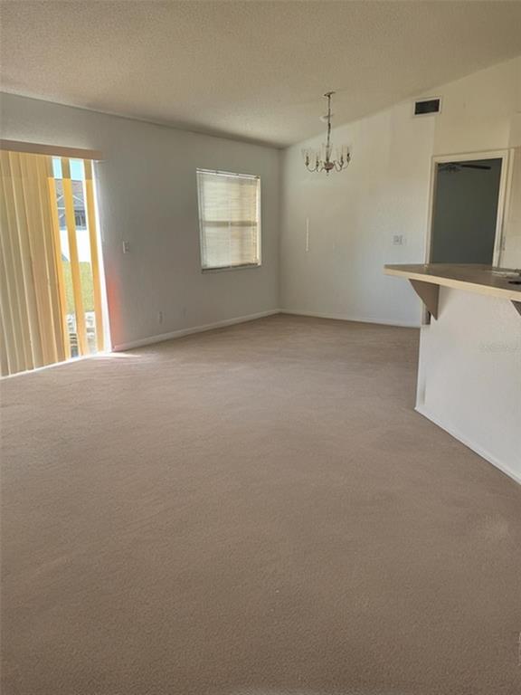This living room features beige carpeting, a sliding glass door, and a breakfast bar — 702 TARTAN LOOP, LAKE WALES, FL