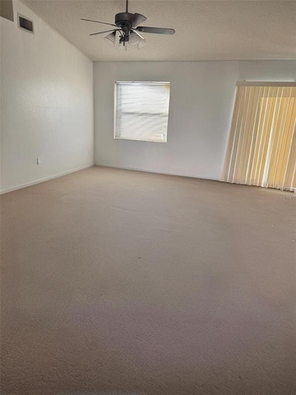 An empty living room features beige carpet, white walls, a ceiling fan, and vertical blinds — 702 TARTAN LOOP, LAKE WALES, FL