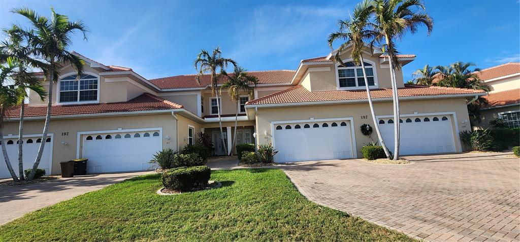 A two-story residential building features a beige stucco exterior, tiled roof, and multiple garage doors — 197 TROPICANA DRIVE UNIT 1512, PUNTA GORDA, FL