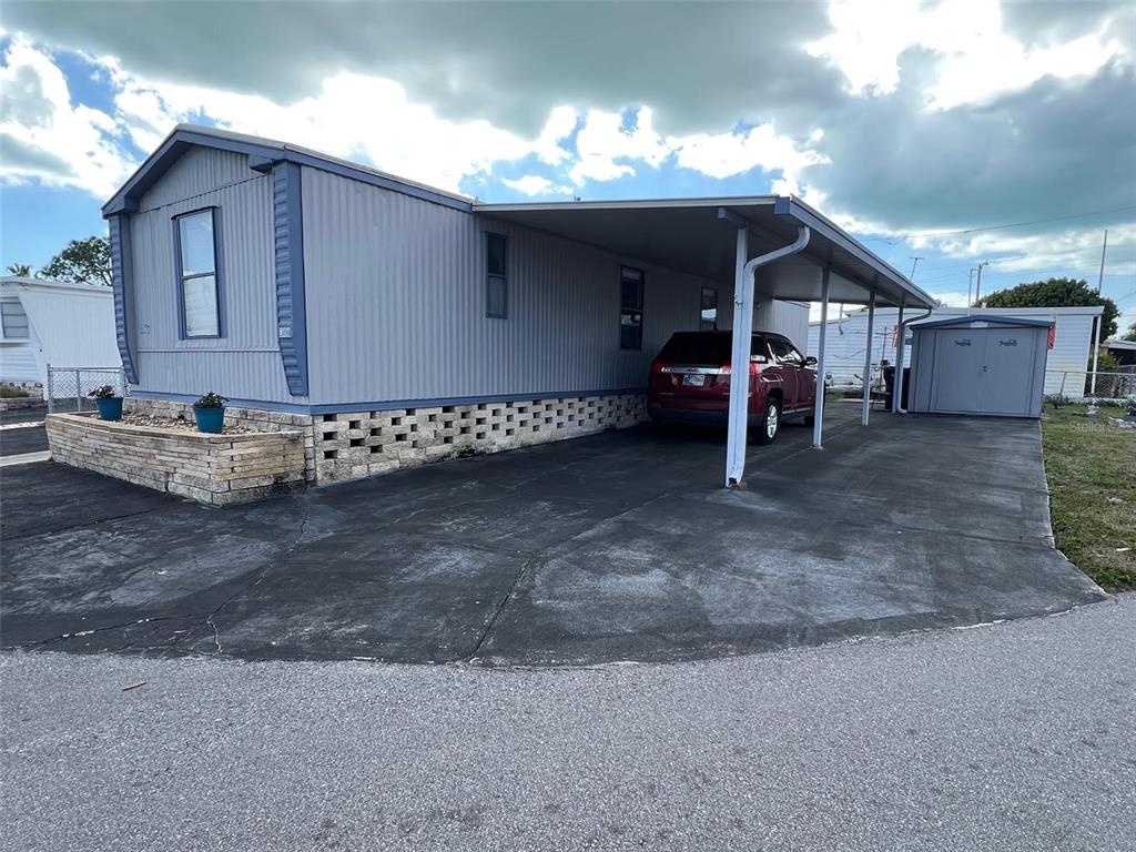 A light blue mobile home features a concrete driveway, a carport, and a stone planter — 6580 SEMINOLE BOULEVARD UNIT 300, SEMINOLE, FL