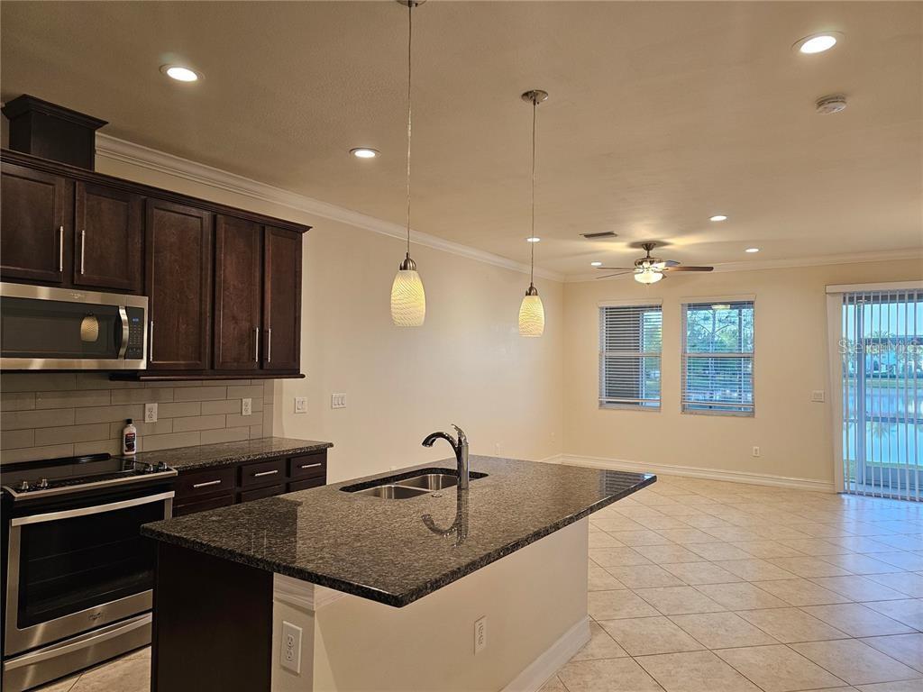 A kitchen with dark wood cabinets, granite countertops, an island, and tile flooring — 3216 PAINTED BLOSSOM COURT, LUTZ, FL