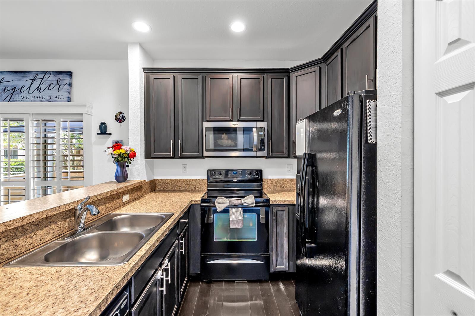 A kitchen features dark wood cabinets, granite countertops, a black refrigerator, and a stainless microwave — 364 Lake Monterey Circle, Boynton Beach FL 33426, BOYNTON BEACH, FL