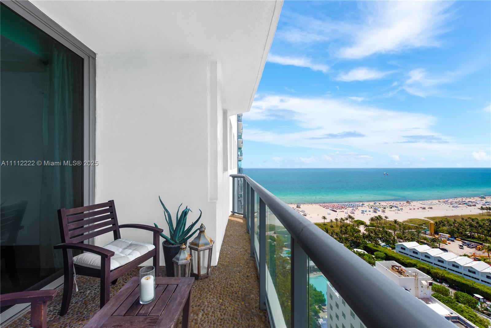 A balcony with a wooden chair and table overlooks the beach and ocean — 101 20th St # 2402, Miami Beach FL 33139, MIAMI BEACH, FL