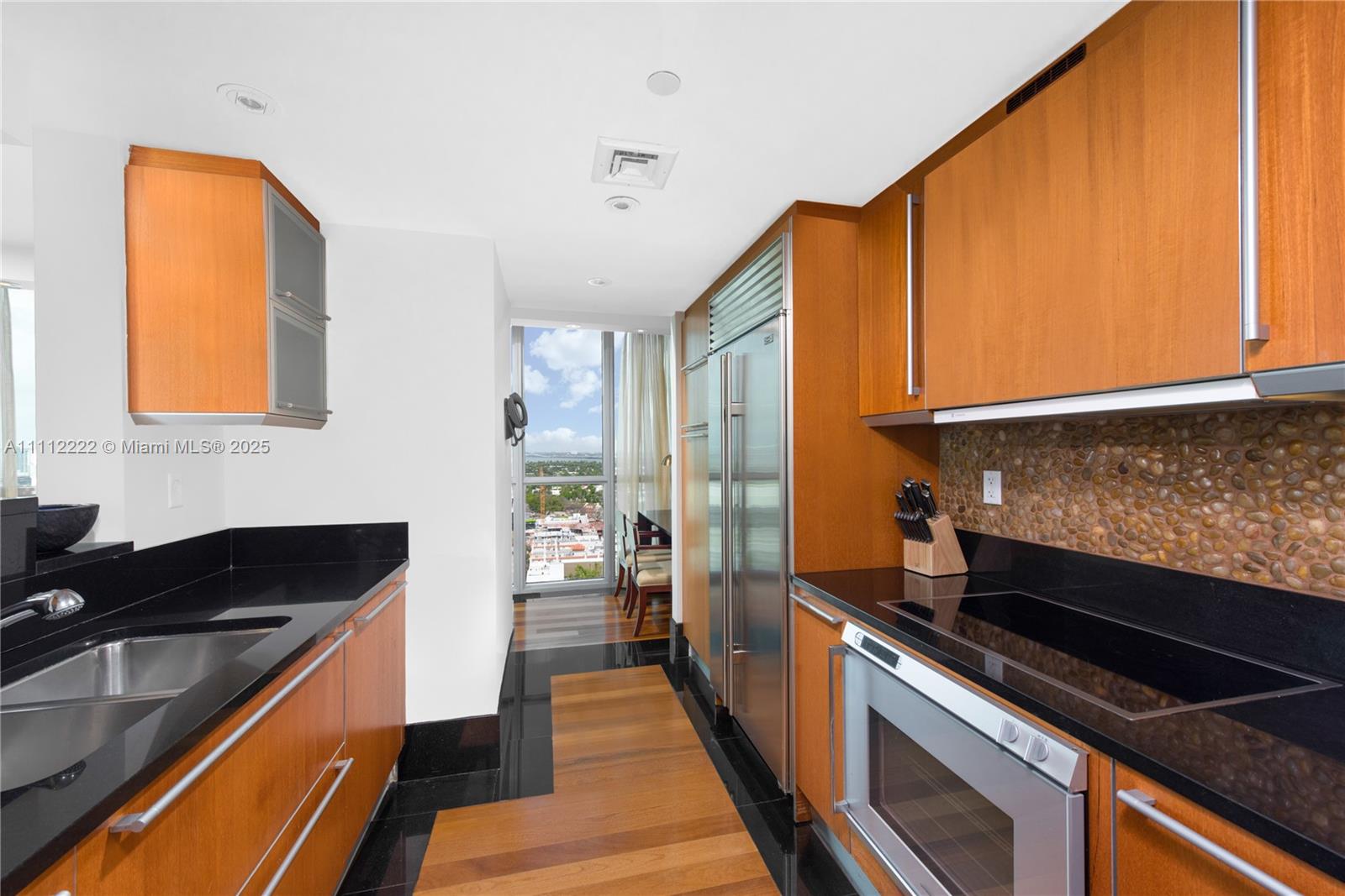 A galley kitchen features wood cabinetry, black countertops, stainless steel appliances, and a city view — 101 20th St # 2402, Miami Beach FL 33139, MIAMI BEACH, FL