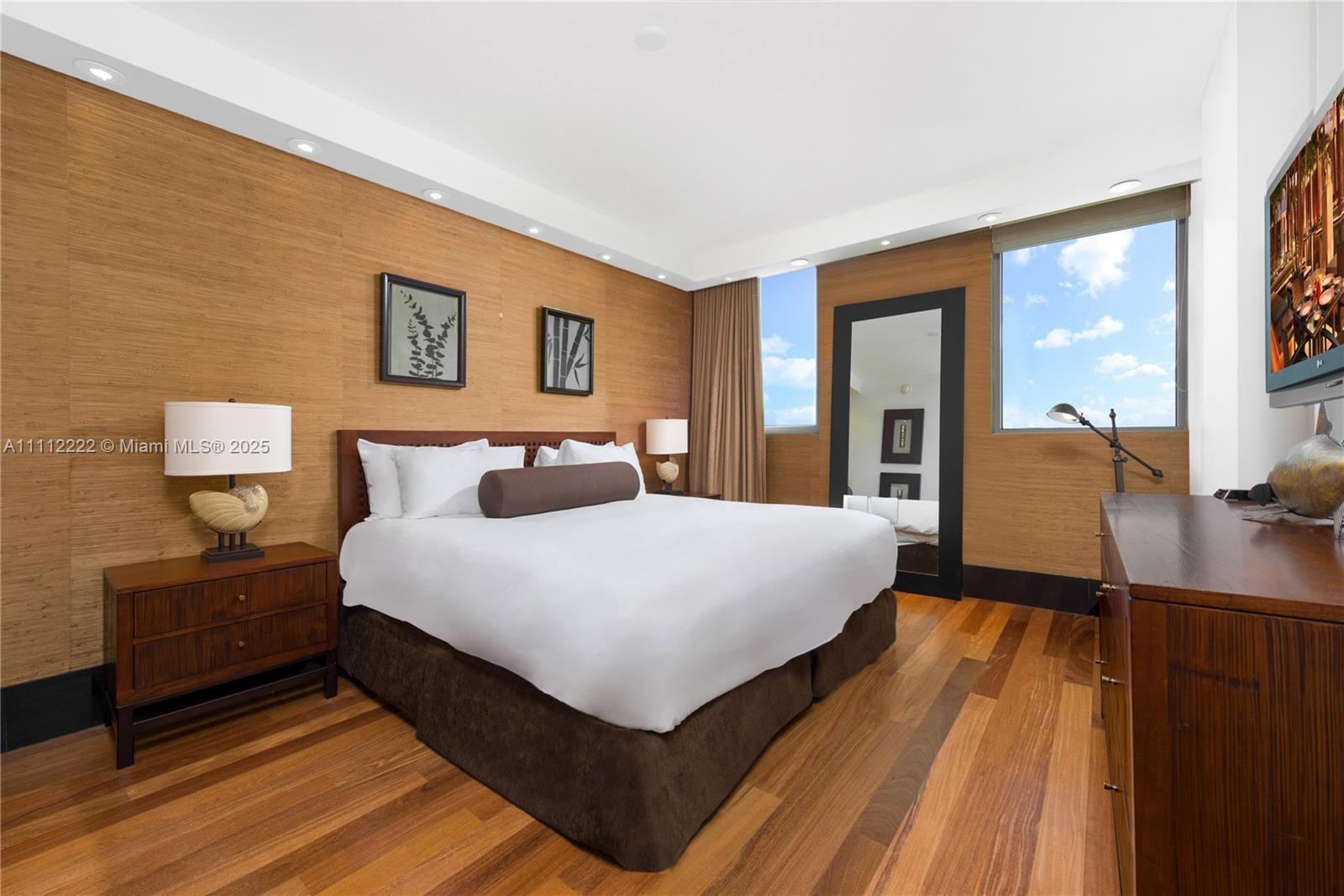 A bedroom features wood-paneled walls, hardwood floors, a king bed, and a large floor mirror — 101 20th St # 2402, Miami Beach FL 33139, MIAMI BEACH, FL