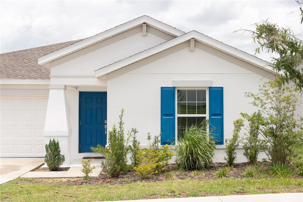 A single-story house with a white stucco exterior, blue shutters, and a blue front door — 707 STAFFORA STREET, HAINES CITY, FL
