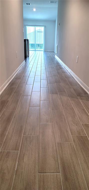 A long hallway with light wood-look tile flooring leads toward a glass sliding door — 707 STAFFORA STREET, HAINES CITY, FL