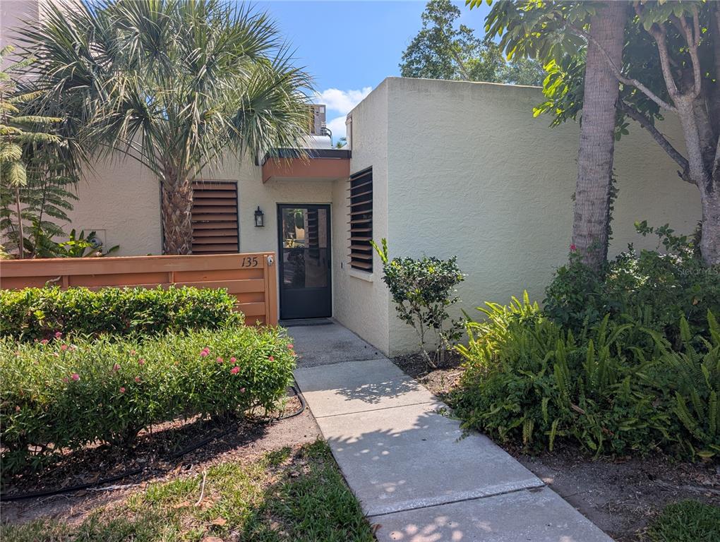 A concrete walkway leads to the front entrance of a stucco home with brown shutters — 135 WILD PALM DRIVE, BRADENTON, FL
