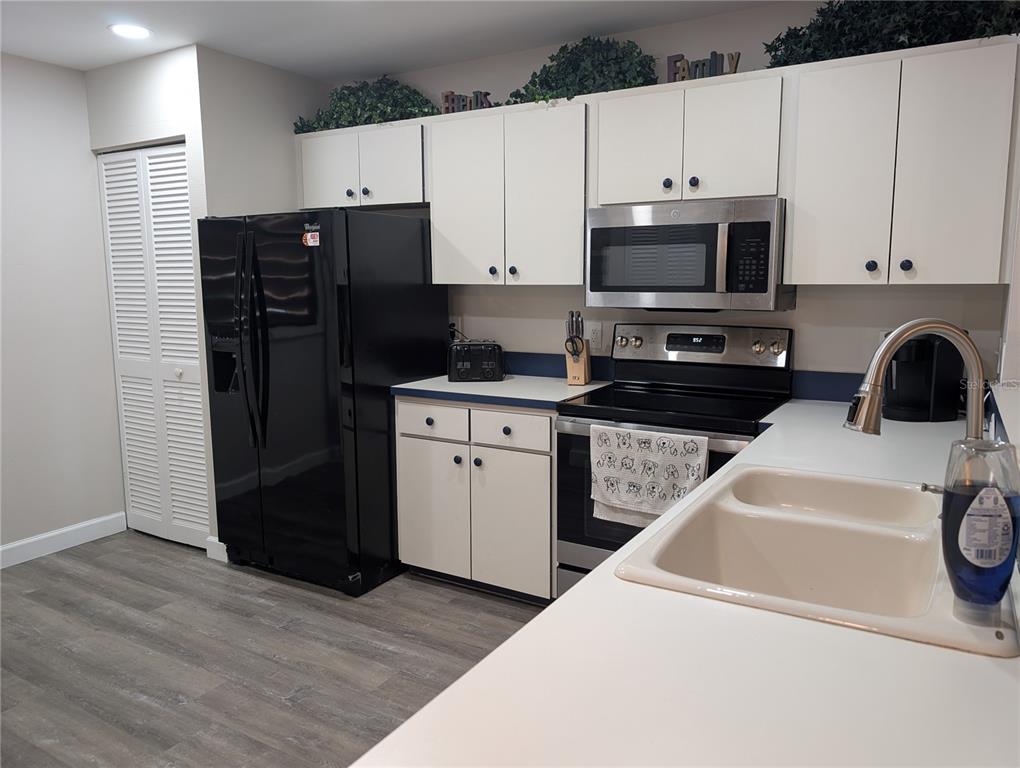 A kitchen features white cabinets, a black refrigerator, stainless steel appliances, and light countertops — 135 WILD PALM DRIVE, BRADENTON, FL