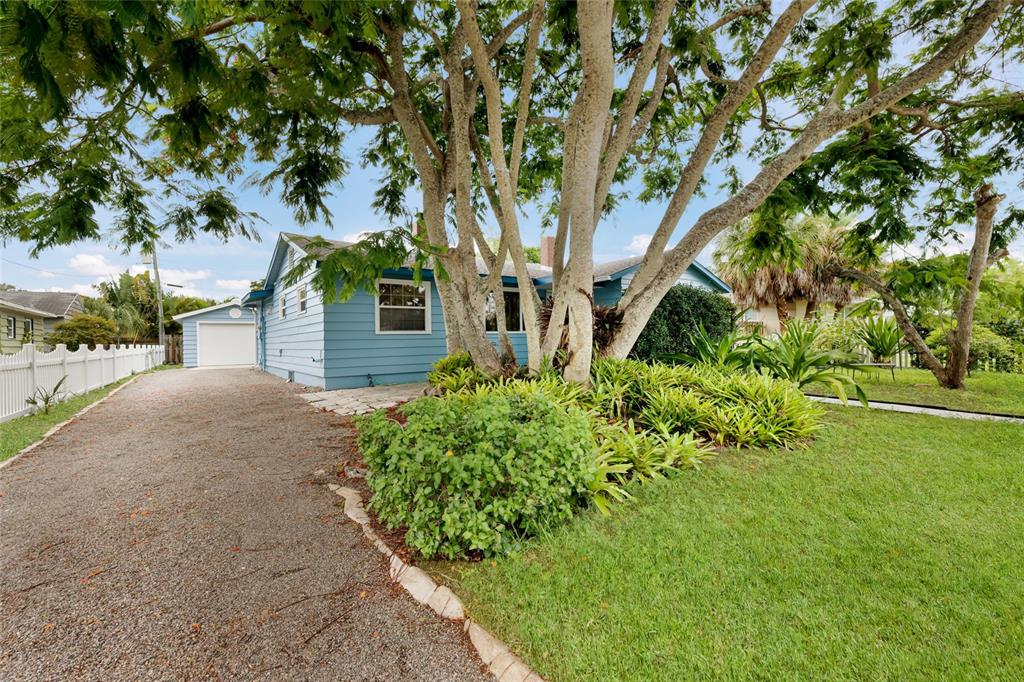 A light blue house with a gravel driveway, large trees, and landscaping in the front yard — 2070 HYDE PARK STREET, SARASOTA, FL
