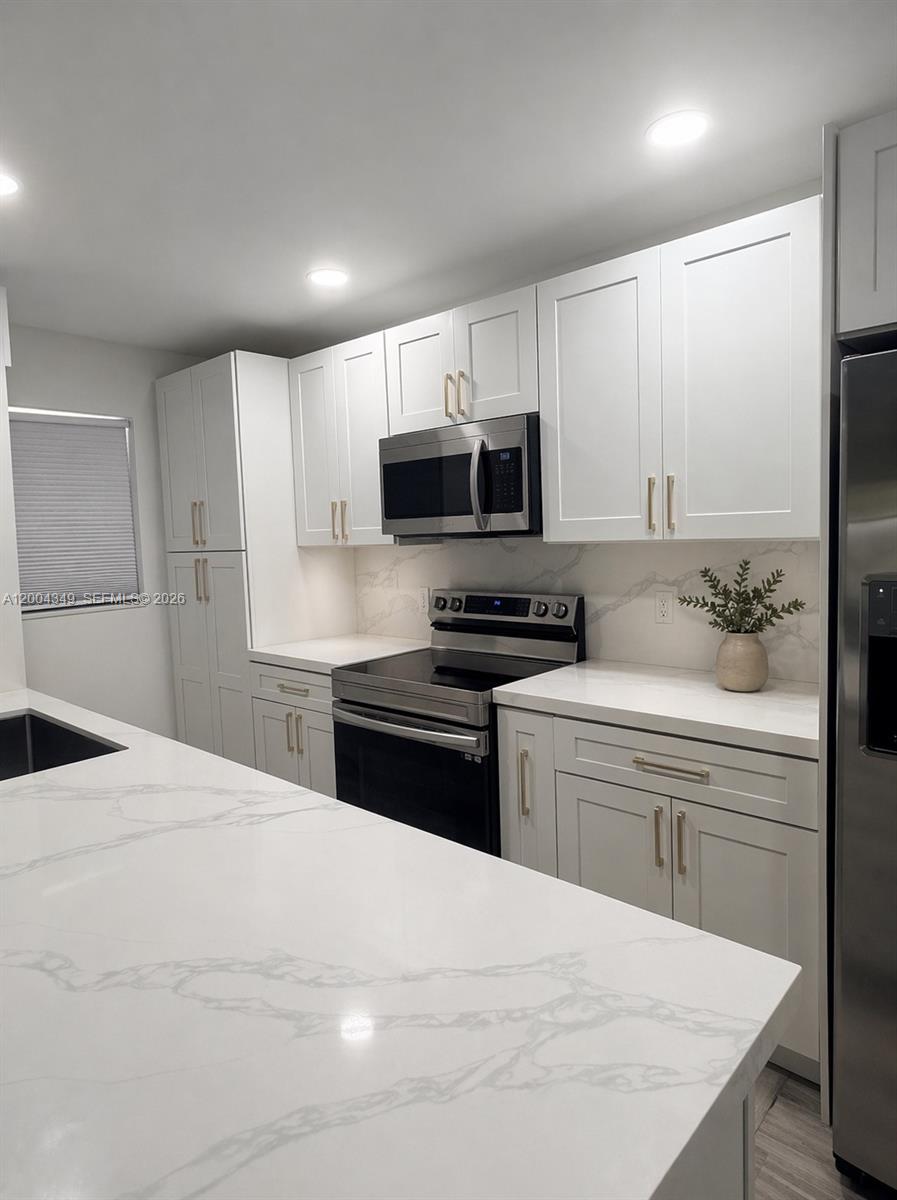A modern kitchen features white shaker cabinets, stainless steel appliances, and white marble-patterned countertops — 200 High Point Ct E # D, Delray Beach FL 33445, DELRAY BEACH, FL