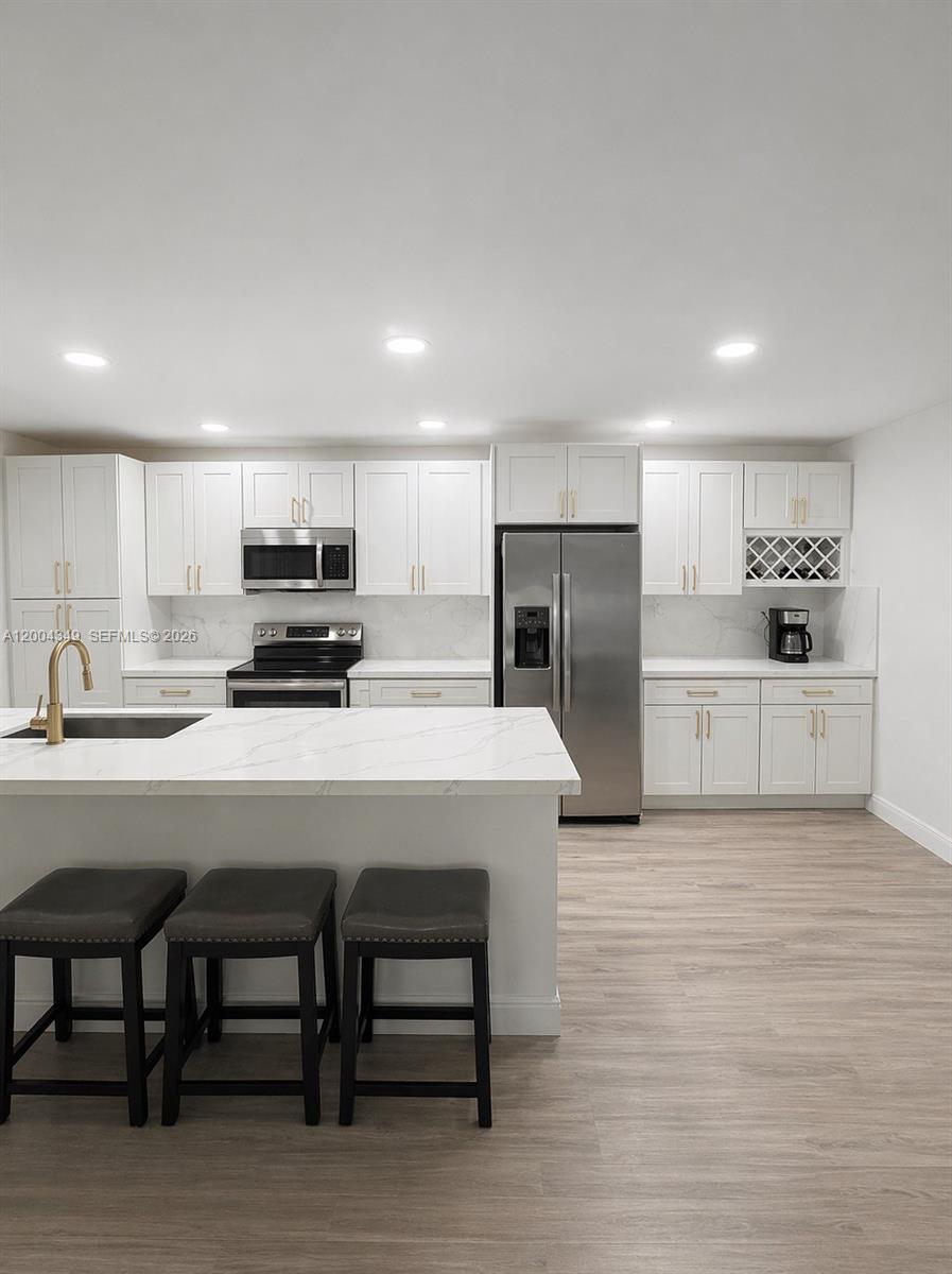 A modern kitchen features white cabinetry, stainless steel appliances, and a large marble-topped island — 200 High Point Ct E # D, Delray Beach FL 33445, DELRAY BEACH, FL