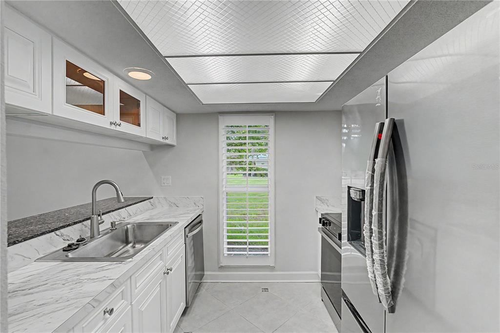 A galley kitchen features white cabinets, marble-look countertops, stainless steel appliances, and a window — 11364 W BAYSHORE DRIVE, CRYSTAL RIVER, FL